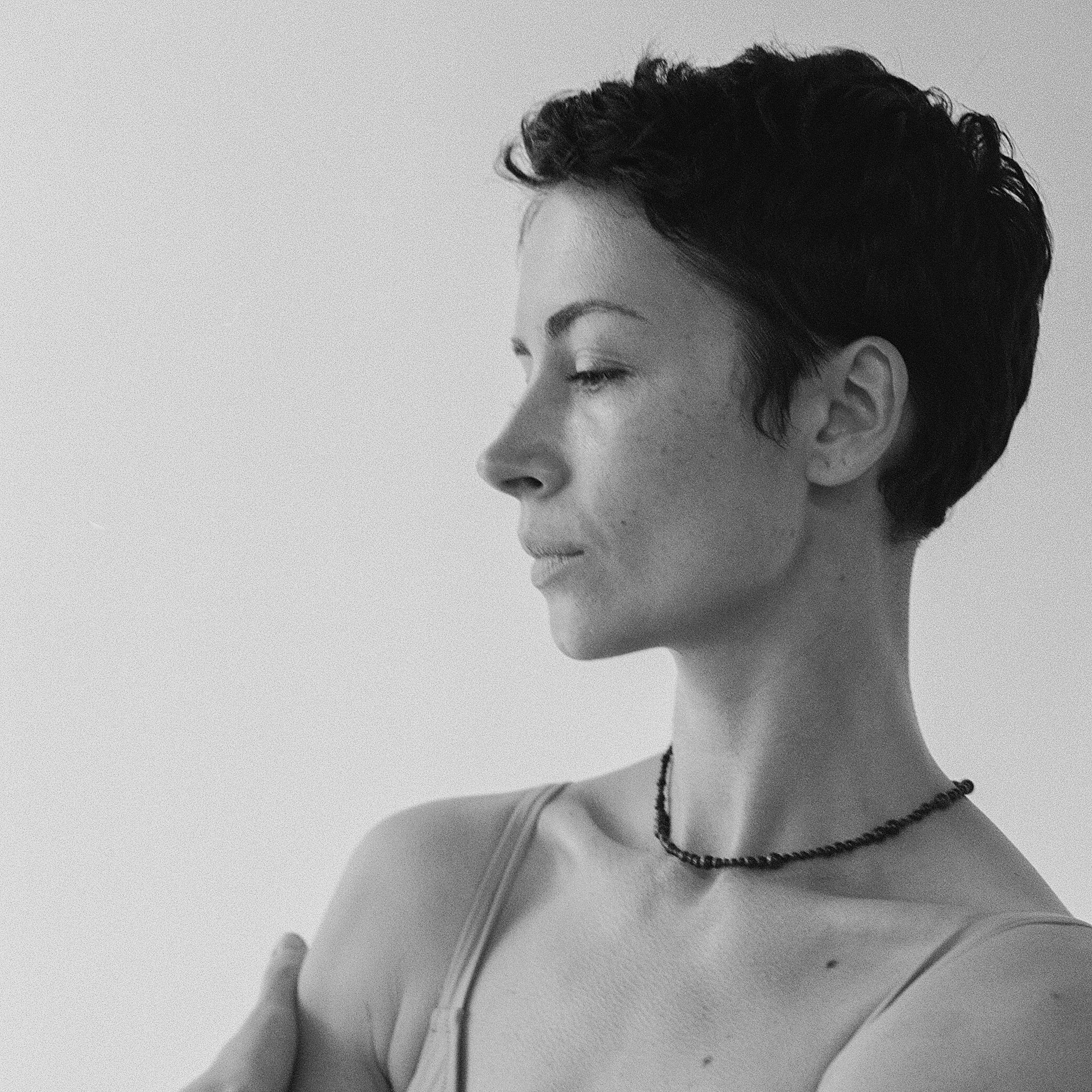Black and white portrait of a woman with short hair and a necklace against a plain background