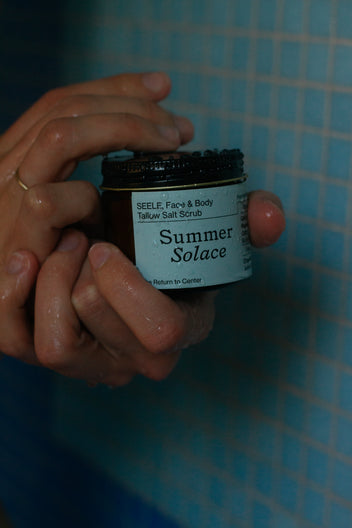 Hand holding a jar of 'Summer Solace' salt scrub against a blue checkered background