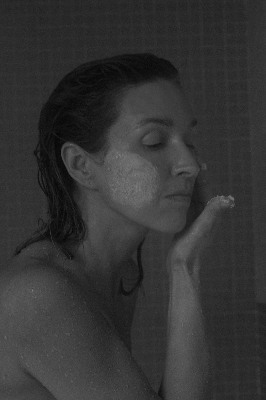 Black and white photo of a woman applying cream to her face.